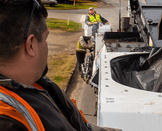 Roadtec SB-3000 Shuttle Buggy Material Transfer Vehicle paving with a Roadtec paver showing a clear line of sight between the two operators