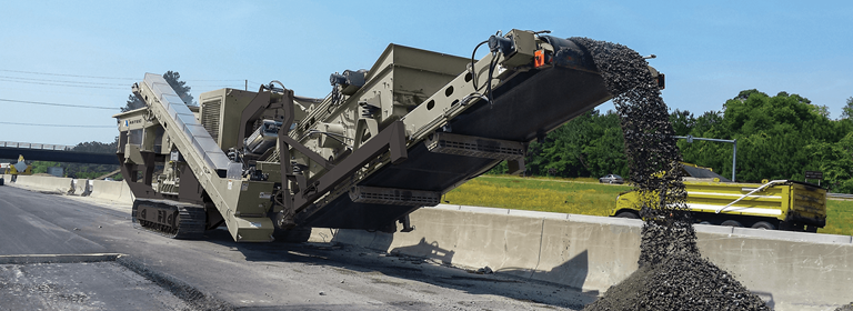 Mobile track-mounted impactor crushing and recycling asphalt from a highway.